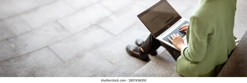 young woman with laptop sitting on the stairs. Person using personal computer outdoors - Powered by Shutterstock