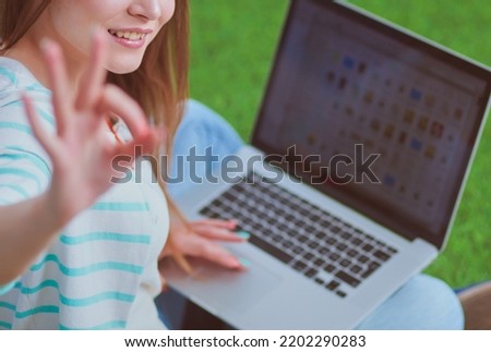 Young woman with laptop sitting on green grass . Portreit young woman