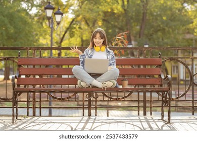 Young woman with laptop video chatting on bench in park - Powered by Shutterstock