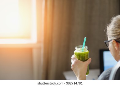 Young Woman With Laptop At Wooden Table. Drinking Green Smoothie