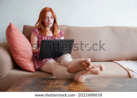 young woman with laptop working from home sitting on sofa with feet on table