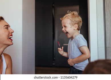 Young Woman Laughing While A Little Boy Putting On Makeup On Her Face. Small Boy Doing Makeup To His Mom And Laughing. Mother And Son Having Fun With Makeup.