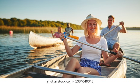 Young woman laughing while paddling a canoe on a scenic lake with a group of friends on a sunny summer afternoon - Powered by Shutterstock