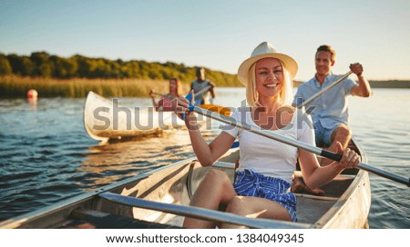 Young woman laughing while paddling a canoe on a scenic lake with a group of friends on a sunny summer afternoon