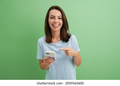 Junge Frau lacht, während sie mit dem Finger auf ihr Handy zeigt einzeln auf grünem Hintergrund