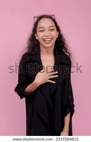 A young woman laughing while putting her hand on her chest, having a great time. Isolated on a light pink background.