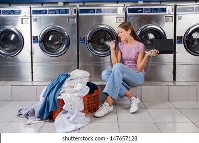 Young woman with laundry basket enjoying music while sitting at laundromat - Powered by Shutterstock