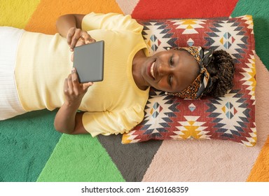 young woman laying down while reading with an e-book - Shutterstock ID 2160168359