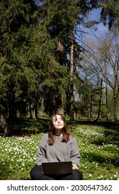 Young Woman Laying In Green Grass Next To The Laptop. People Fatigue From Work. Sleeping And Relaxation Techniques. Vitamin D Sunbathing. Female Power Nap With Eye Closed. Rest After Work From Home