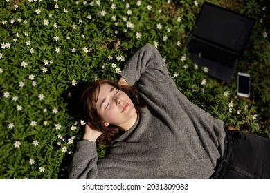 Young Woman Laying In Green Grass Next To The Laptop. People Fatigue From Work. Sleeping And Relaxation Techniques. Vitamin D Sunbathing. Female Power Nap With Eye Closed. Rest After Work From Home