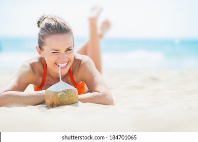 Young woman laying on beach and drinking coconut milk