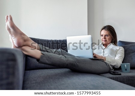 Young woman laying on the couch using laptop. European female working on computer at home.