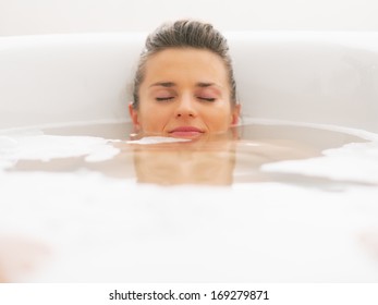 Young woman laying under water in bathtub