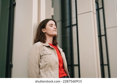 Young woman leaning against a modern house facade and relaxing with closed eyes - Shutterstock ID 2287560915