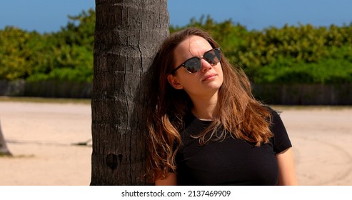 Young Woman Leaning Against A Palm Tree At Miami Beach