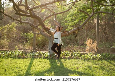 Young Woman Leaning Against A Plum Tree. Full Length Portrait Of A Mexican Woman Leaning Against A Plum Tree At Sunset.