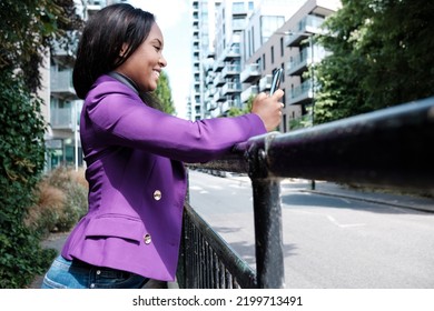 A Young Woman Is Leaning On A Banister And Using A Mobile Phone. She Is On A London Street, Texting On Her Phone.