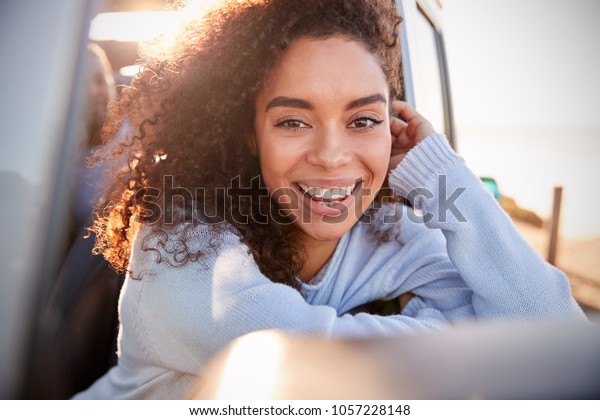 Young woman leaning on open window of car looking\
to camera