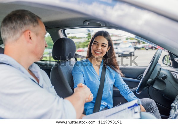 Young woman\
learning how to drive car together with her instructor. Driving\
school. Happy driving student.  Woman passed. Young woman delighted\
having just passed her driving\
test