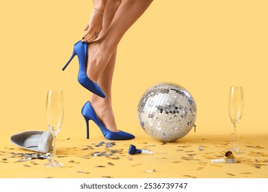 Young woman legs with disco ball and party decor on yellow background. New Year celebration - Powered by Shutterstock