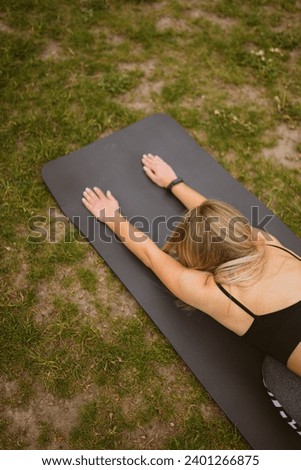 Young woman lies in fetal position straightening posture on mat on lawn. Lady in sportswear does yoga to relieve tension from muscles