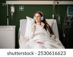 Young woman lies in a hospital room, enjoying music through her headphones.