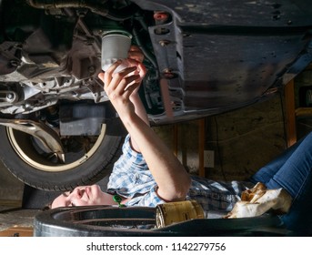 A Young Woman Lies On Garage Floor Replacing The Oil Filter On Her Car After Performing Routine Oil Change