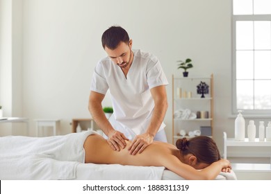 Young woman lies on a massage table during a wellness body massage session in a massage parlor. Slender male masseur massages the back of a young girl in a modern medical center.