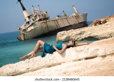 A Young Woman Lies On A Rock Against The Backdrop Of Abandoned Ship Edro III Near Cyprus Beach. Rusty Ship Ran On The Ground Near The Shore. Old Stranded Ship. Paphos. Cyprus. Limassol. 