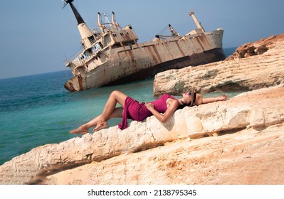 a young woman lies on a rock against the backdrop of Abandoned ship Edro III near Cyprus beach. Rusty ship ran on the ground near the shore. old stranded ship. paphos. Cyprus. Limassol. 