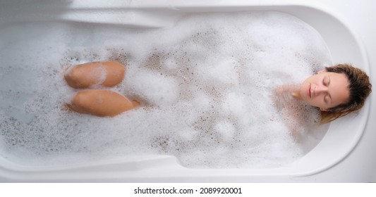 A young woman lies in a soapy foam bath, top view - Powered by Shutterstock