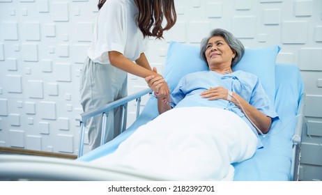 Young Woman Lifting A Railing Beside The Bed And Holding His Sick Mother's Hand To Get Saline On The Bed In The Hospital Room. Daughter Encouraging Mother Lying Sick In The Patient Room.