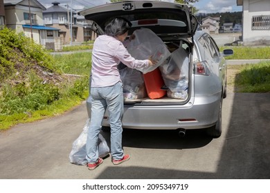 A Young Woman Is Lifting Trash Bag And  Into Trunk Of A Car