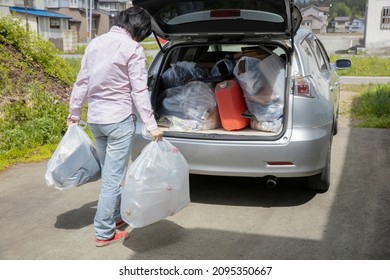 A Young Woman Is Lifting Trash Bag And  Into Trunk Of A Car