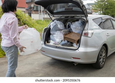 A Young Woman Is Lifting Trash Bag And  Into Trunk Of A Car