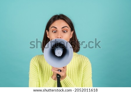 Young woman in light green sweater with megaphone funny screaming playful