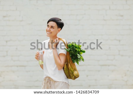Young woman in light summer clothes with a eco bag of vegetables, greens and reusable water bottle.  Sustainable lifestyle. Eco friendly concept.