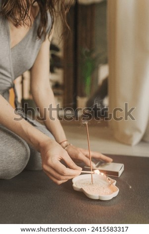 A young woman lighting incense sticks an home before yoga. Buddhist healing practices. Clearing the space of negative energy. Aromatherapy. Selective focus.