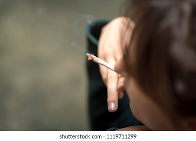 Young woman lighting a rolled joint of marihuana, closeup, smoking weed