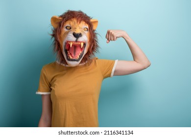 Young woman in lion mask flexing arm muscles, isolated on blue background with copy-space.