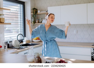 Young woman listening music and enjoying cup of coffee at morning, in her kitchen. - Powered by Shutterstock