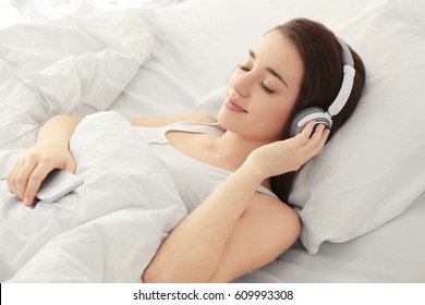 Young Woman Listening To Music In Headphones On Bed