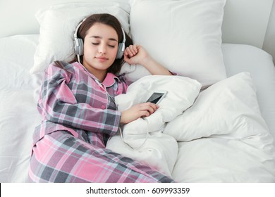 Young Woman Listening To Music In Headphones On Bed