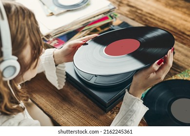 Young woman listening to music from vinyl record player. Playing music on turntable player. Female enjoying music from old record collection at home. Stack of analog vinyl records. Retro and vintage - Powered by Shutterstock