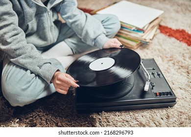 Young Woman Listening To Music From Vinyl Record Player. Retro And Vintage Music Style. Girl Holding Analog Record Album Sitting In Room At Home. Female Enjoying Music From Old Record Collection