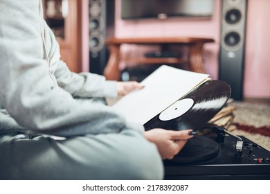 Young woman listening to music from vinyl record player. Retro and vintage music style. Girl holding analog record album sitting in room at home. Female enjoying music from old record collection - Shutterstock ID 2178392087