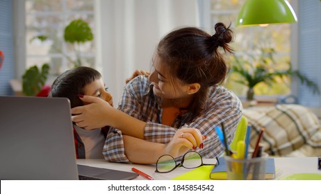 Junge Frau mit kleinen Kindern arbeitet am Computer. Cute Preschool Junge umarmt Mutter sitzend am Schreibtisch und arbeitet im Büro zu Hause. Arbeiten vom daheim- und Fernbildungskonzept