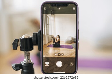 Young woman with little daughter fitness blogger doing exercises and recording video on mobile phone in studio - Powered by Shutterstock