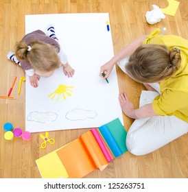 Young Woman And Little Girl Drawing Together Sitting On The Floor. Top View