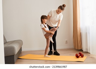 Young Woman With Little Girl Wearing Sportswear Doing Sport Exercises At Home, Kid Standing With One Leg Lift, Thighs Workout, Warming Up Training Muscles, Child Having Workout With Trainer.